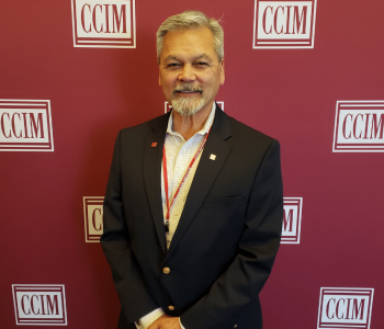 A Man Wearing A Suit And Tie Standing In Front Of A Sign