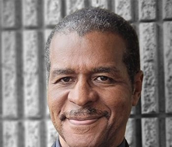 A Man Wearing A Suit And Tie Smiling And Looking At The Camera