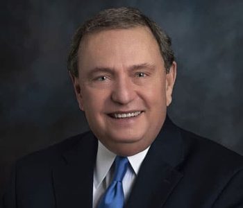 A Man Wearing A Suit And Tie Smiling At The Camera