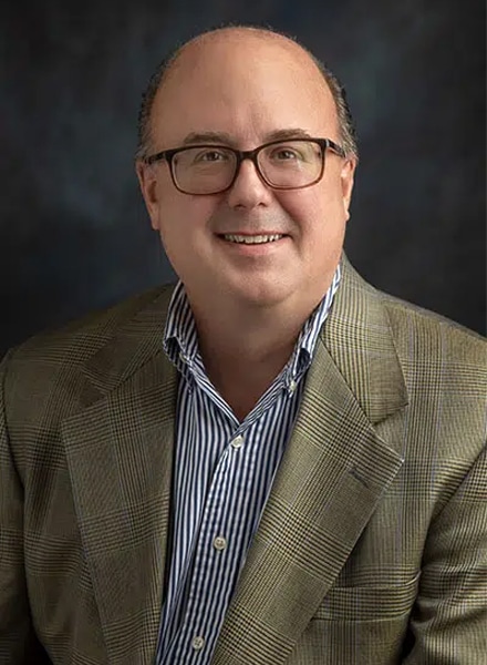 a man wearing a suit and tie smiling at the camera