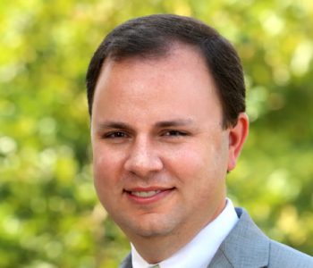 A Man Wearing A Suit And Tie Smiling At The Camera