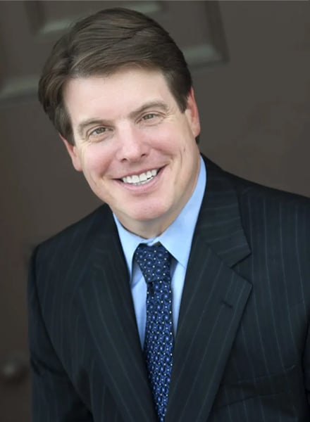 a man wearing a suit and tie smiling at the camera