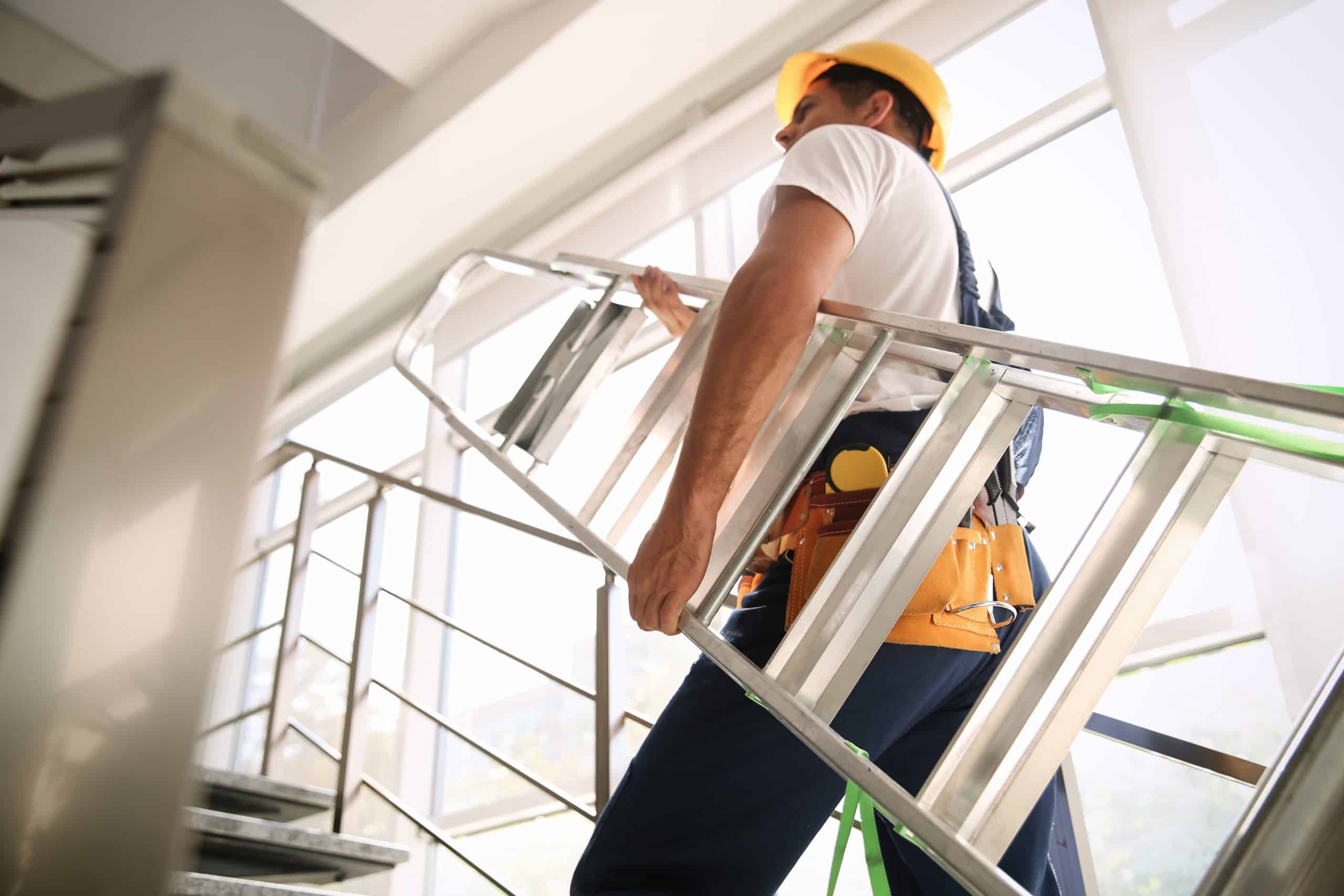 Professional builder carrying metal ladder up stairs, low angle