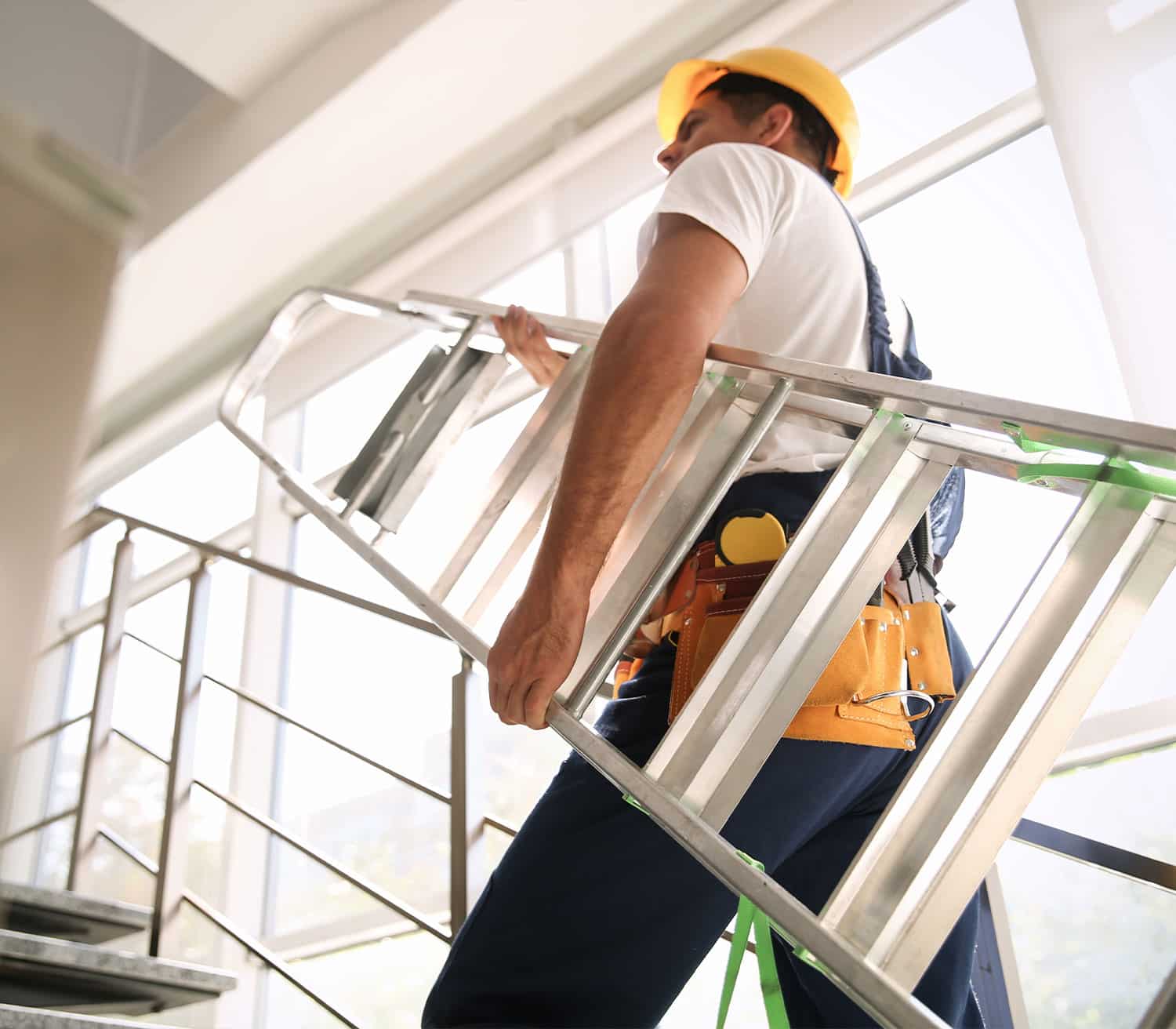 A maintenance man walks up the stairs with a ladder.